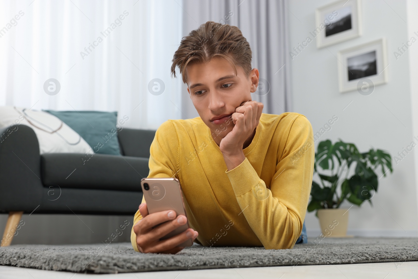 Photo of Young man with smartphone on carpet indoors