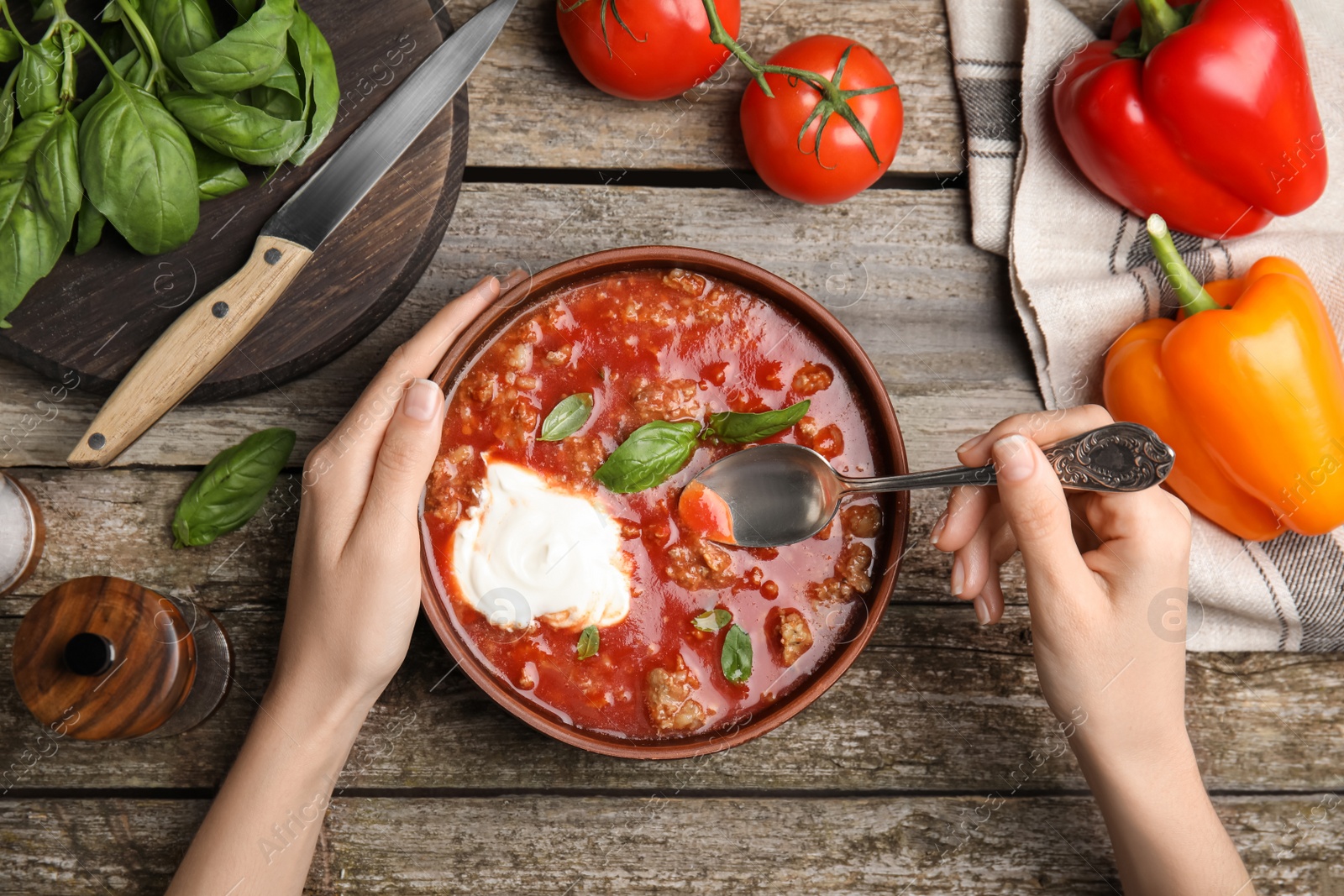 Photo of Woman with bowl of delicious stuffed pepper soup at wooden table, top view