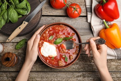 Photo of Woman with bowl of delicious stuffed pepper soup at wooden table, top view