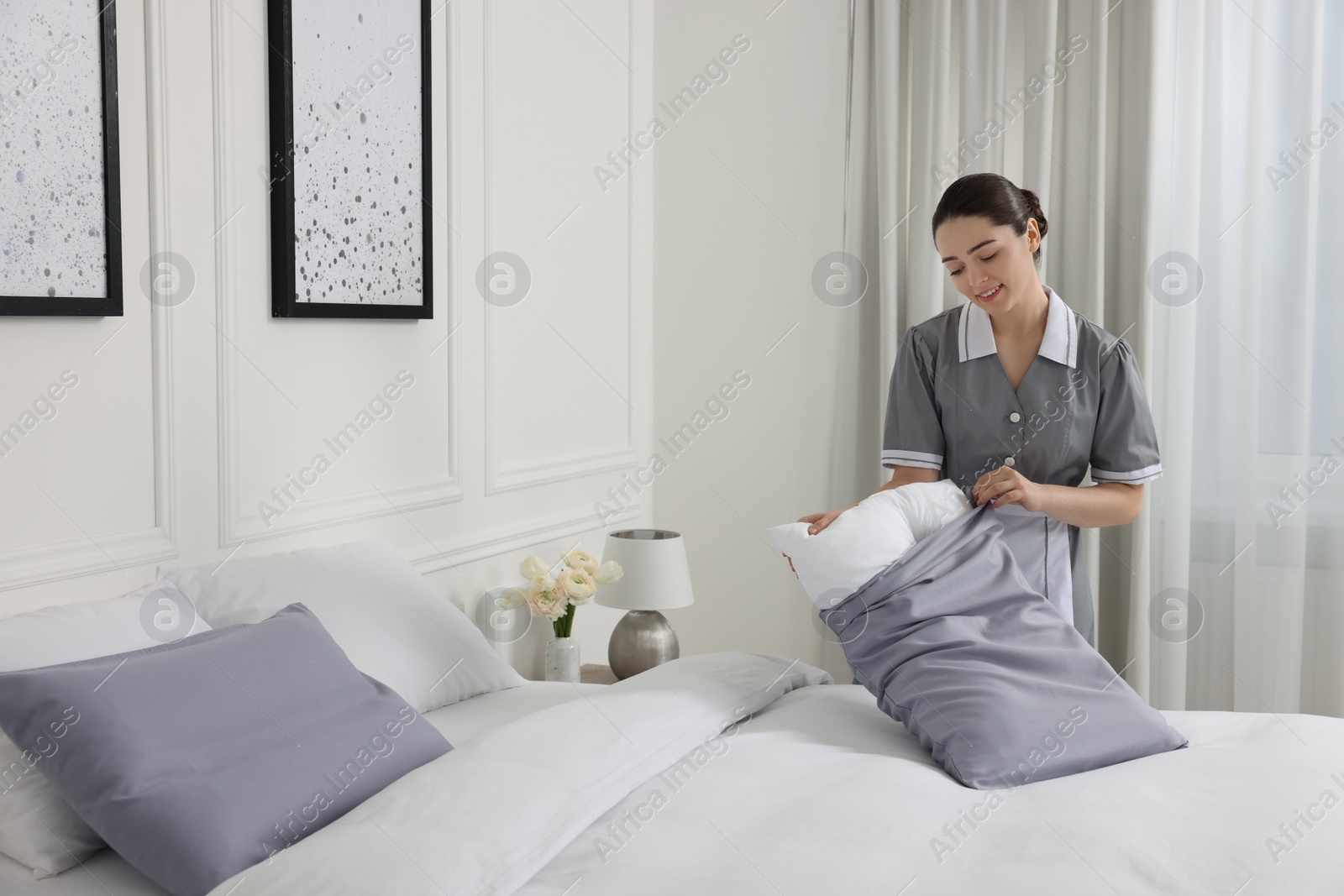 Photo of Young maid making bed in hotel room. Space for text