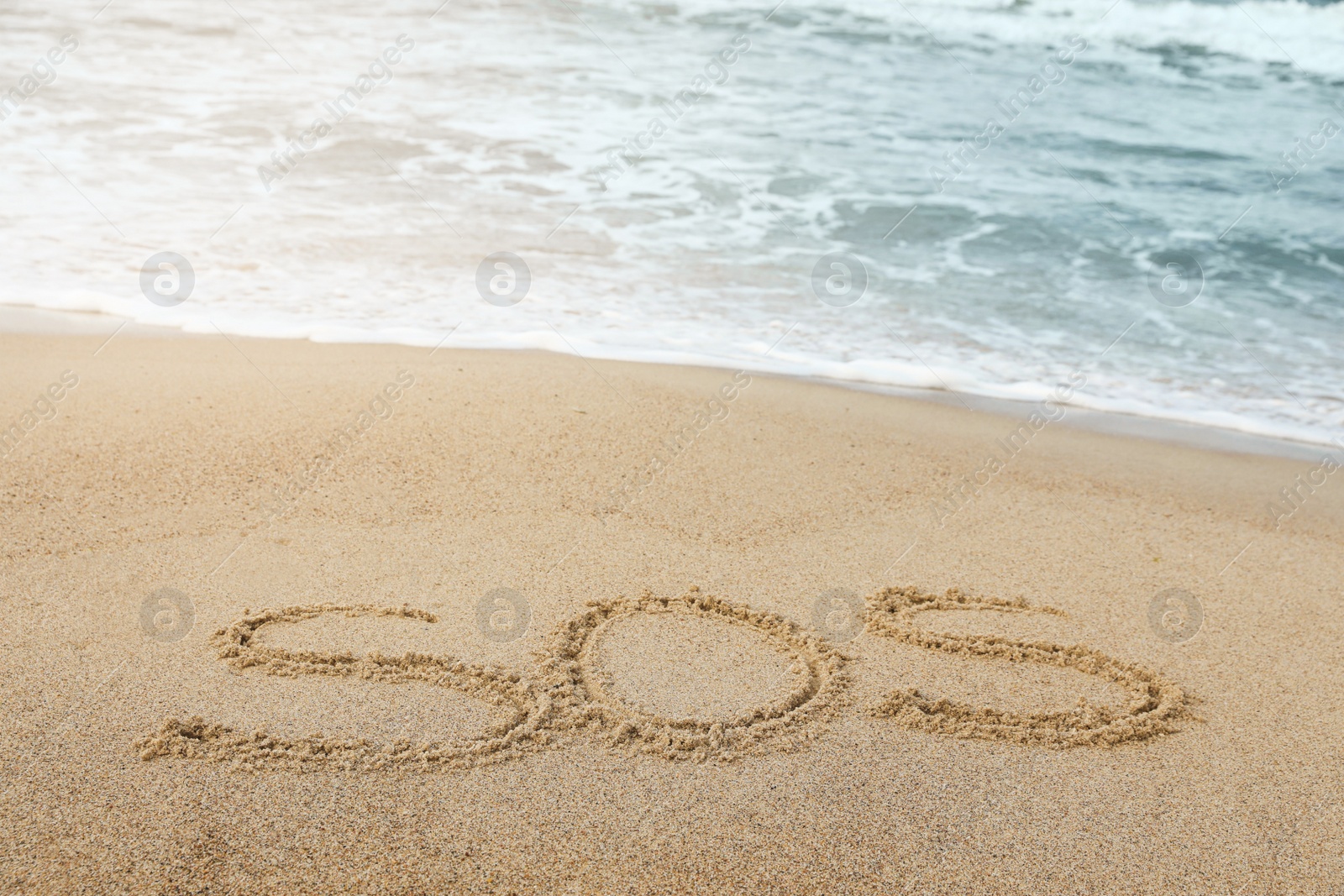 Photo of Message SOS drawn on sand near sea