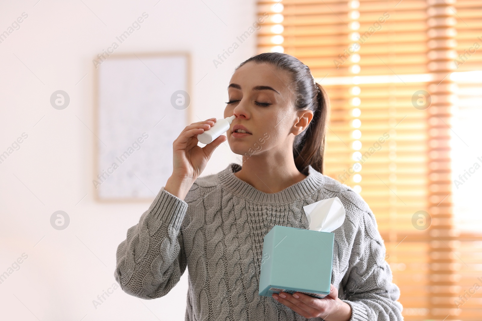 Photo of Ill woman with box of paper tissues using nasal spray at home
