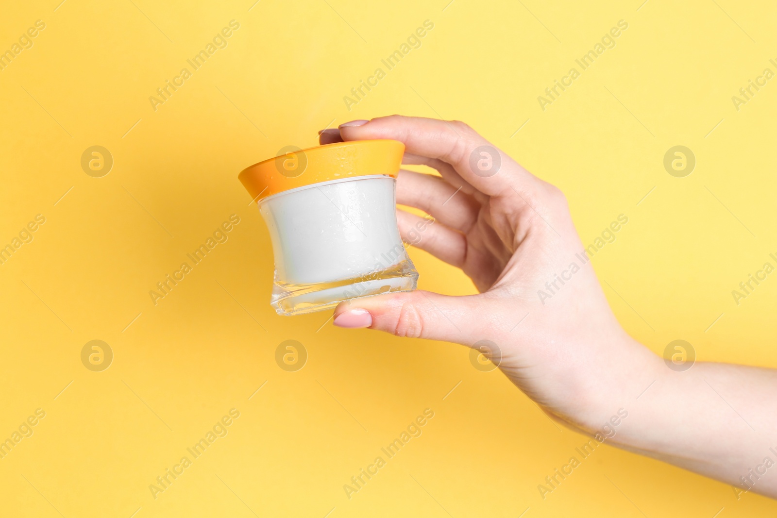 Photo of Woman holding jar of cream on yellow background, closeup