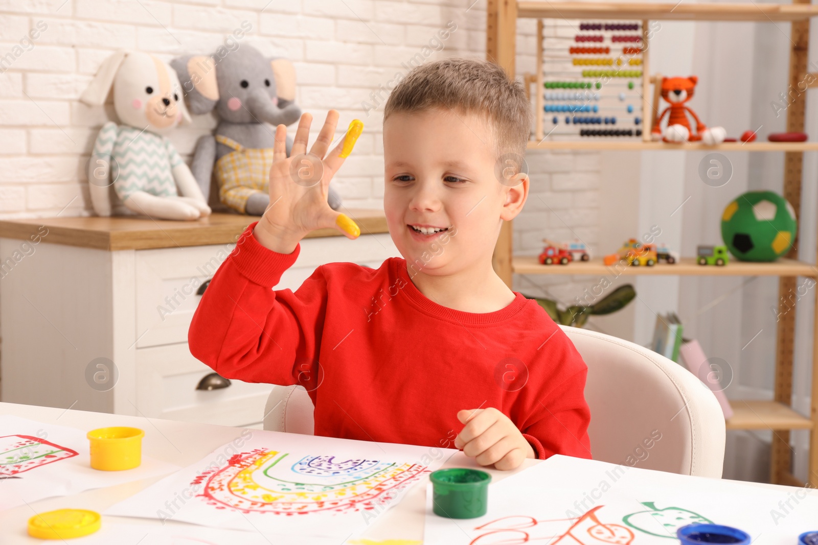 Photo of Little boy painting with fingers at white table indoors