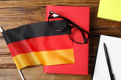 Photo of Learning foreign language. Flag of Germany, book, glasses and stationery on wooden table, flat lay