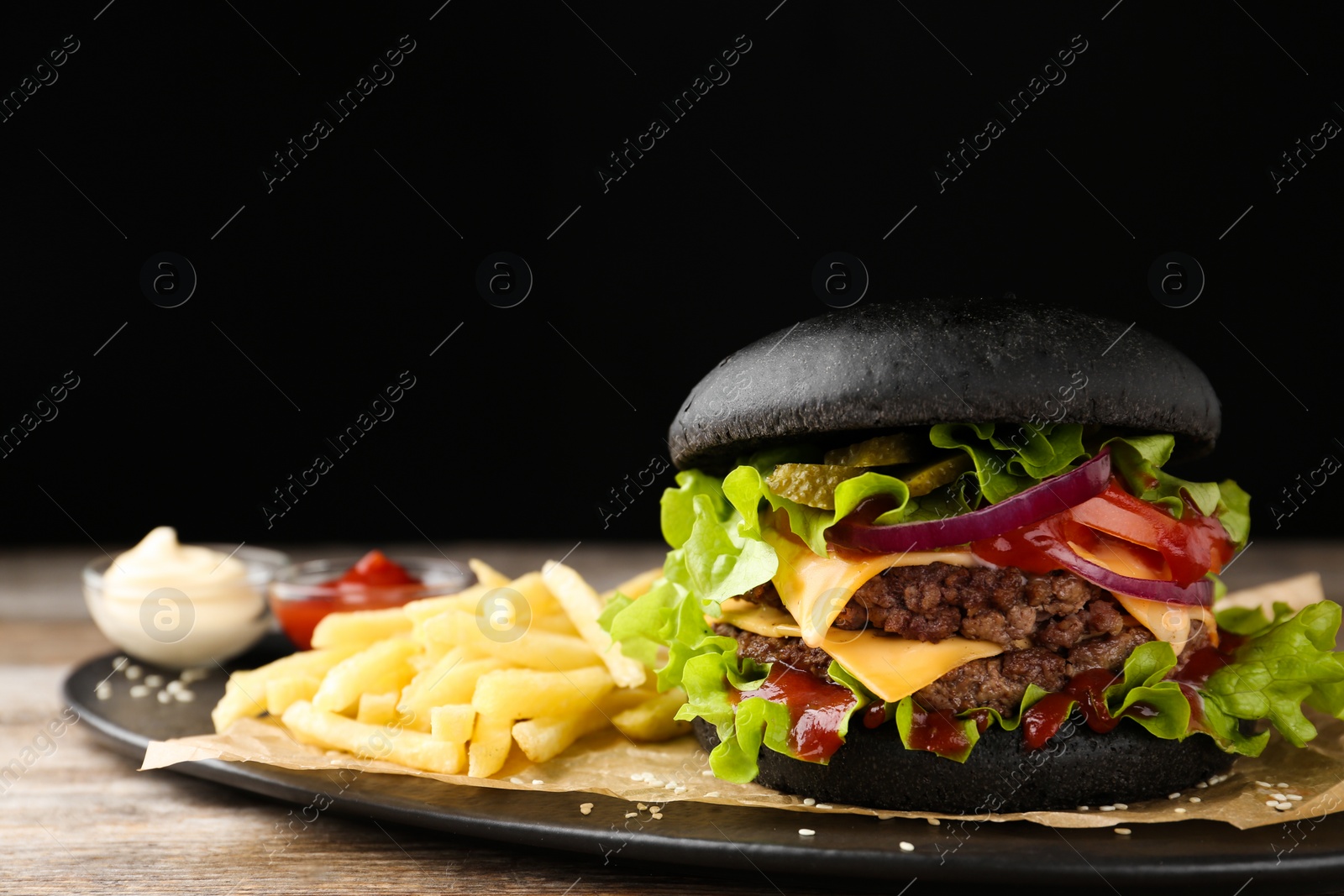 Photo of Plate with black burger and French fries on table, closeup. Space for text