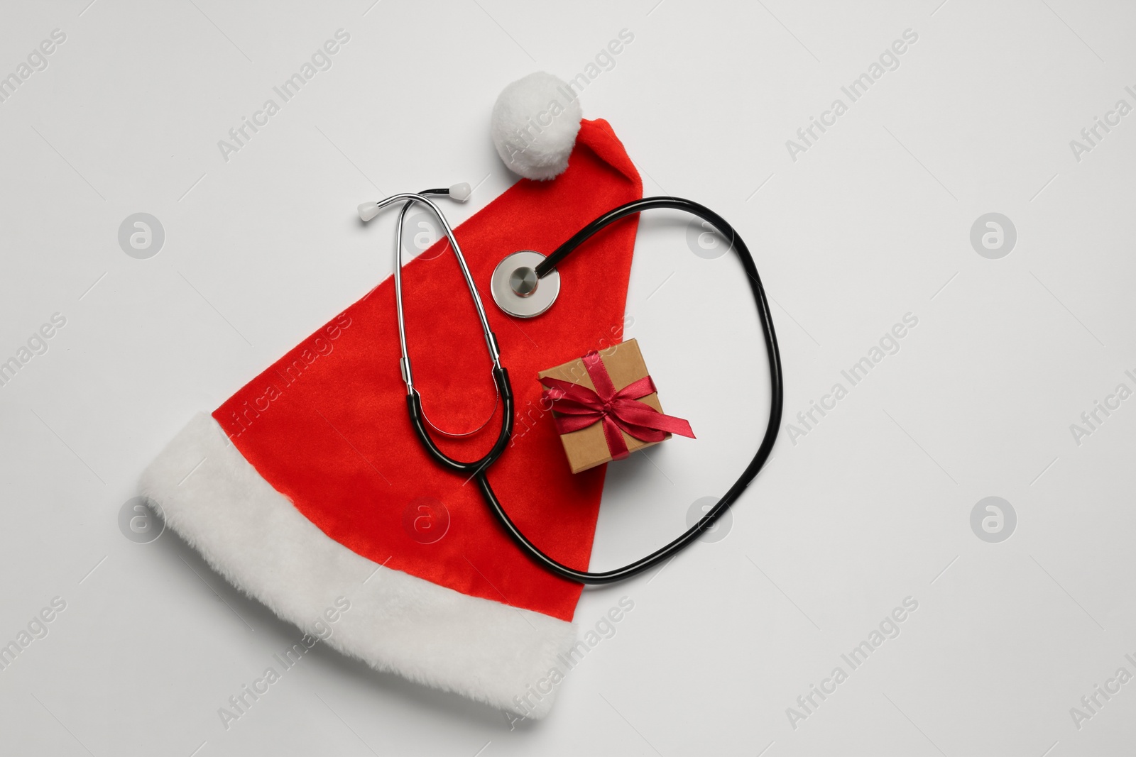 Photo of Greeting card for doctor with stethoscope, gift boxes and Santa hat on white background, top view. Space for text