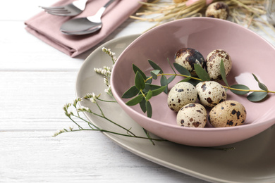 Festive Easter table setting with quail eggs and floral decor on wooden background, closeup