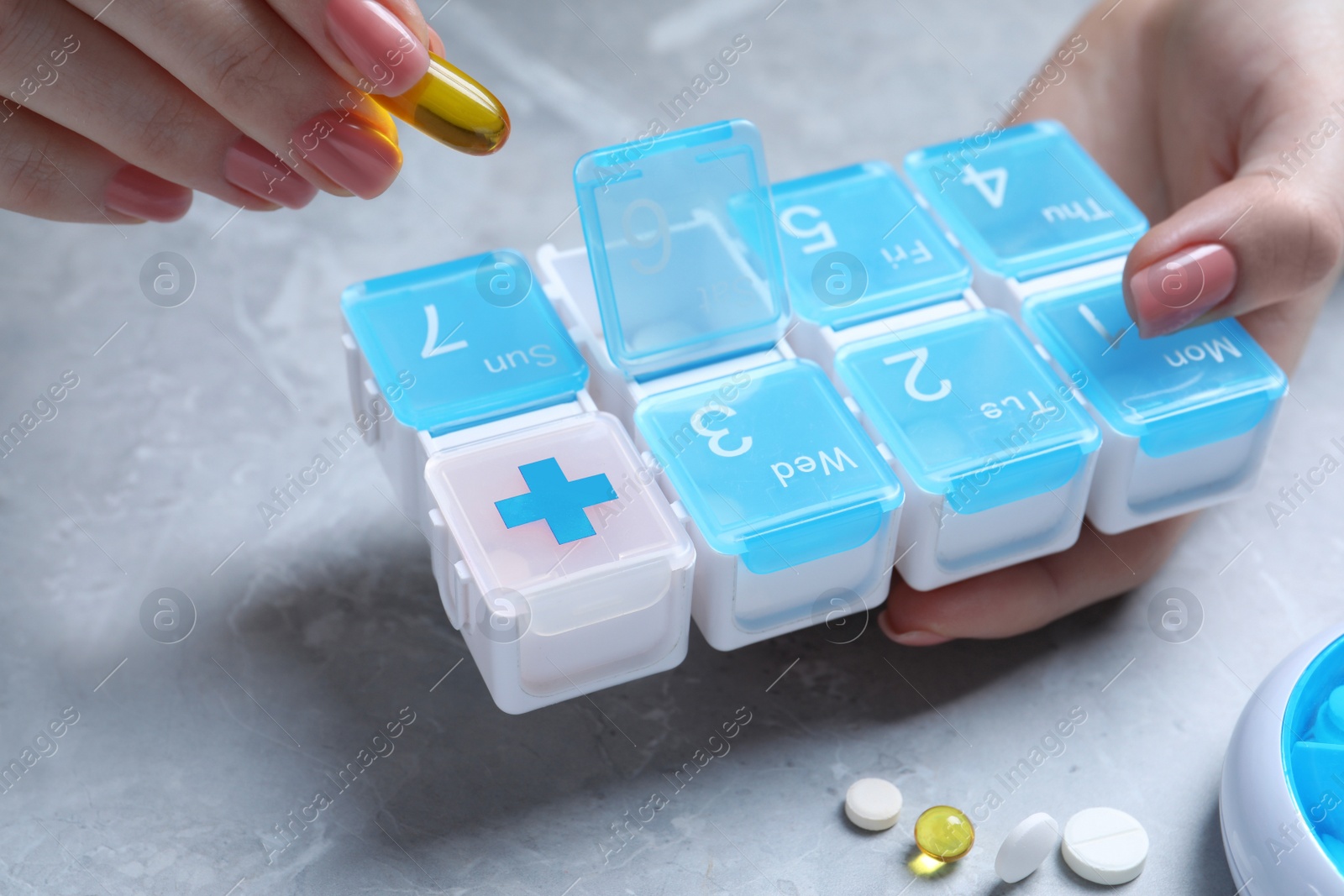 Photo of Woman putting pill into plastic box at grey marble table, closeup