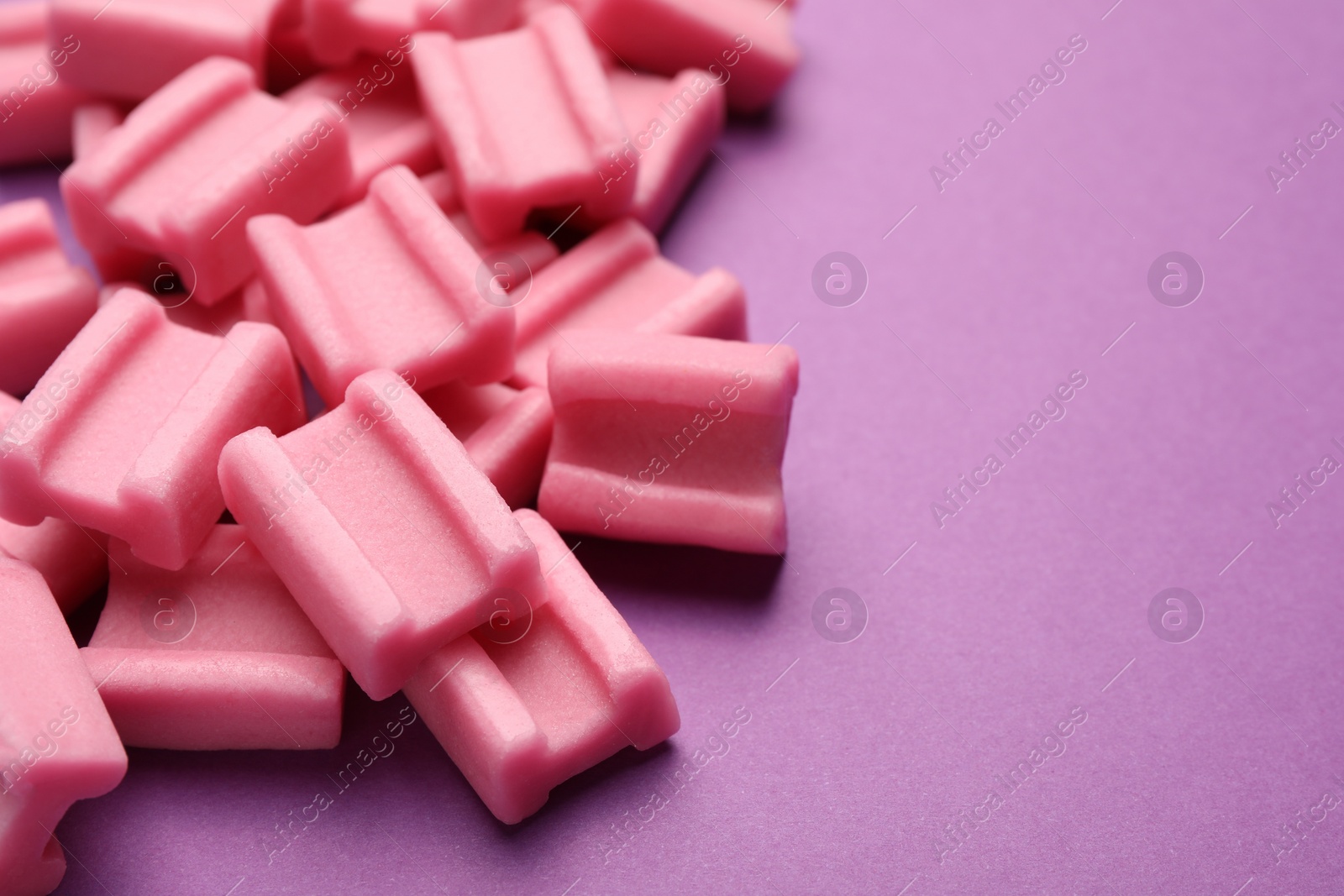 Photo of Tasty pink chewing gums on purple background, closeup. Space for text