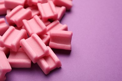 Photo of Tasty pink chewing gums on purple background, closeup. Space for text