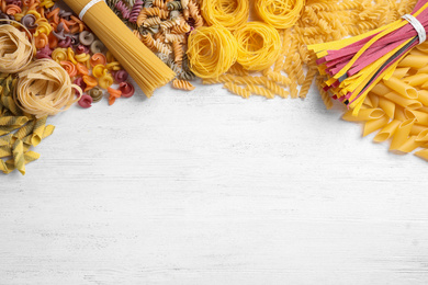 Photo of Different types of pasta on white wooden table, flat lay. Space for text