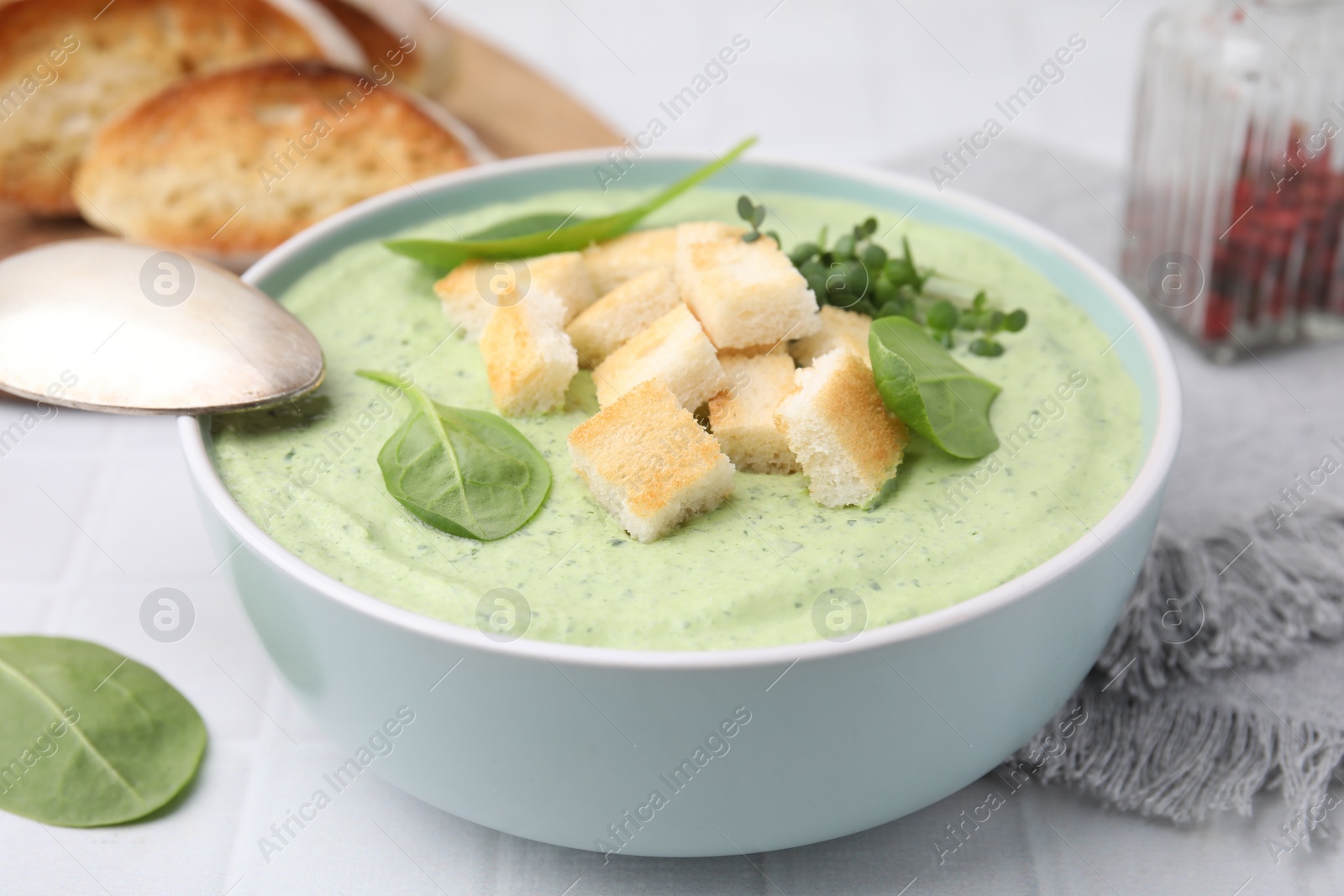 Photo of Delicious spinach cream soup with croutons in bowl on white tiled table