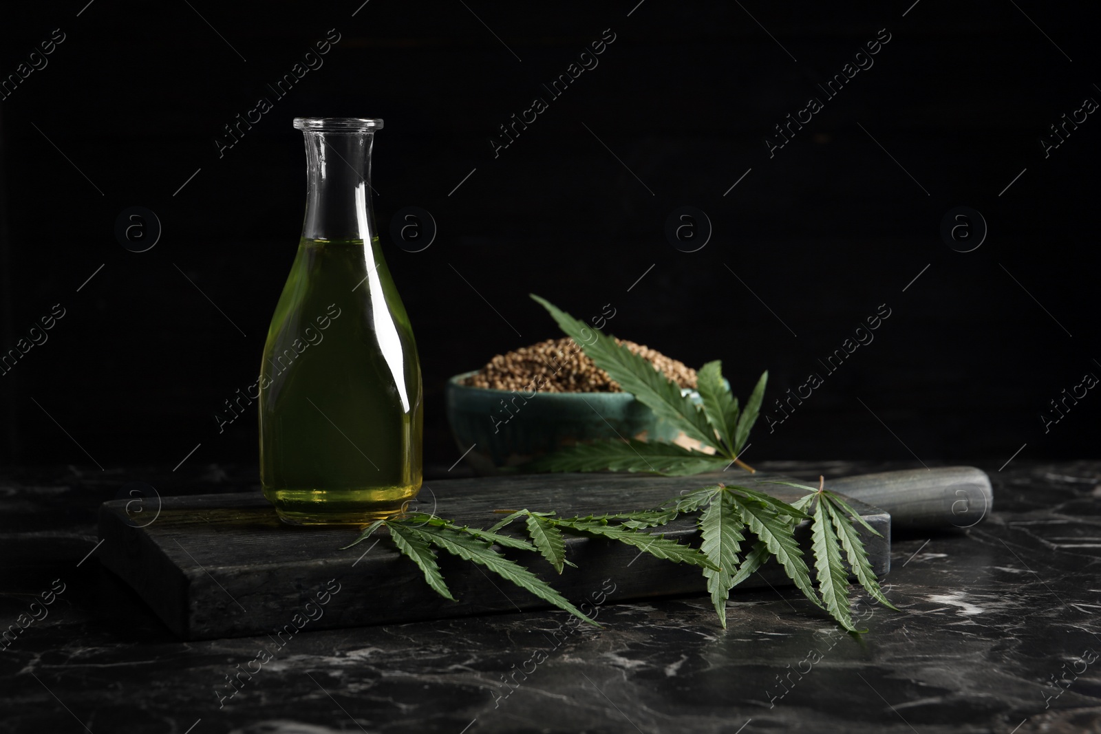 Photo of Bottle with hemp oil and fresh leaves on dark table. Space for text