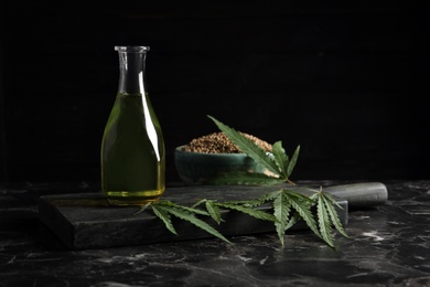 Bottle with hemp oil and fresh leaves on dark table. Space for text