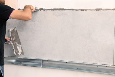 Photo of Worker spreading adhesive mix on wall for tile installation indoors, closeup