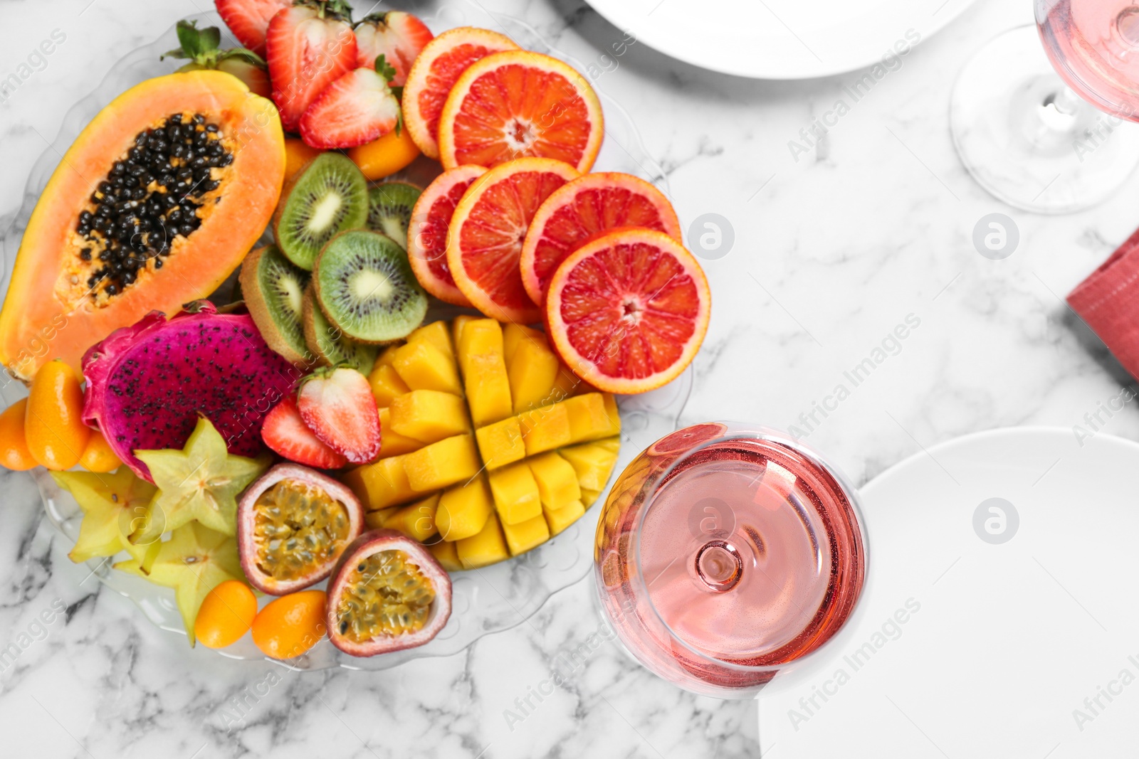 Photo of Delicious exotic fruits and wine on white marble table, flat lay
