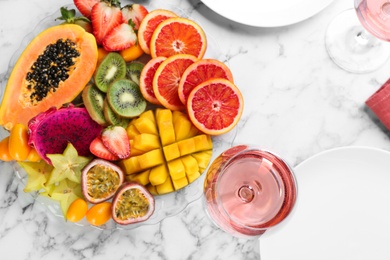 Delicious exotic fruits and wine on white marble table, flat lay