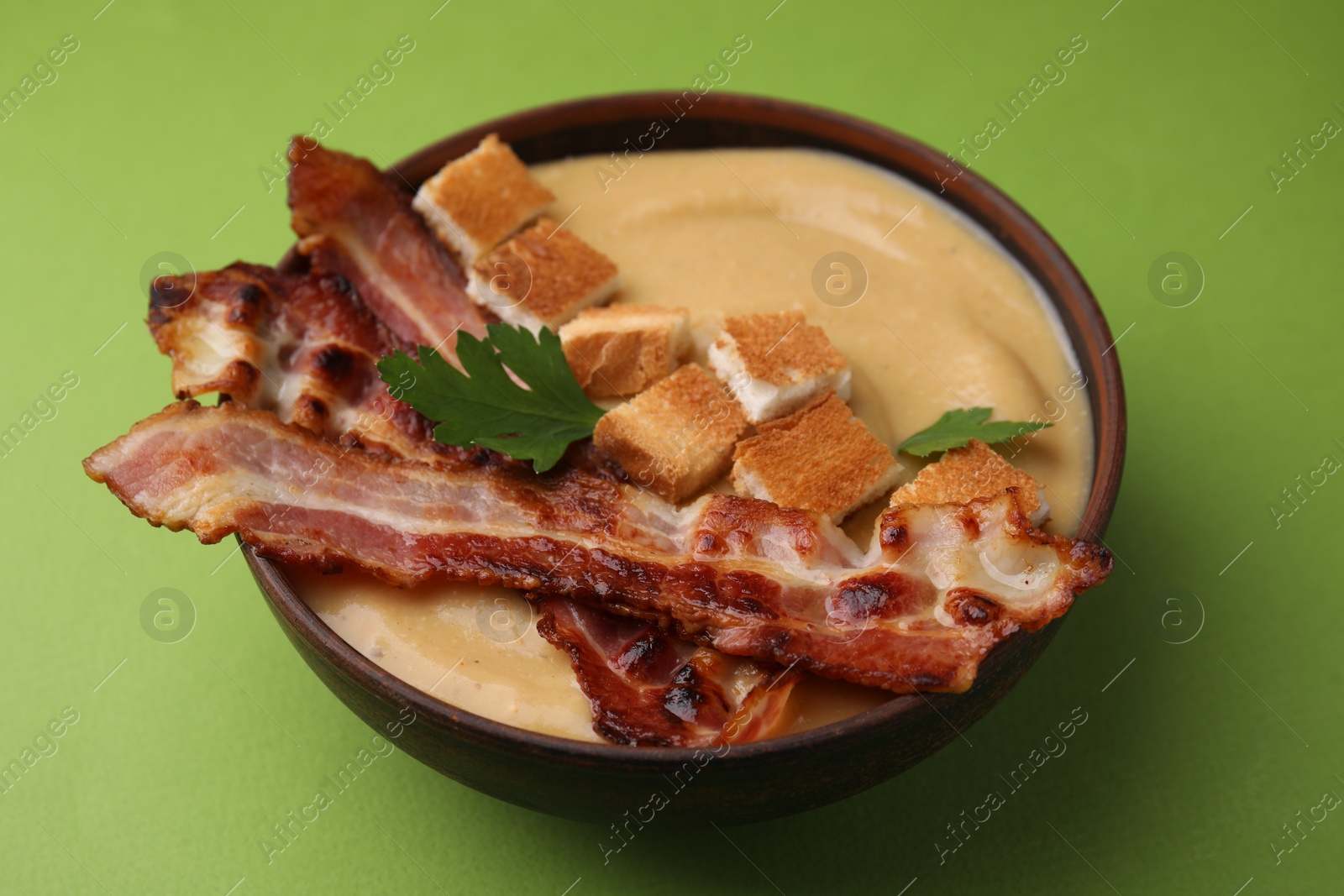 Photo of Delicious lentil soup with bacon and parsley in bowl on green table, closeup