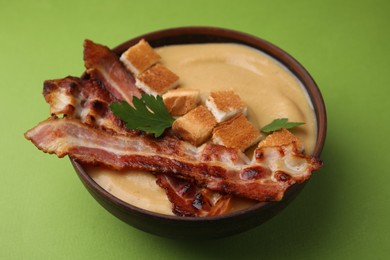 Delicious lentil soup with bacon and parsley in bowl on green table, closeup