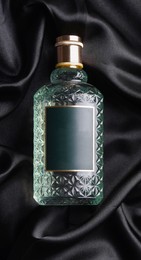 Photo of Luxury bottle of perfume on black silk, top view
