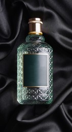 Luxury bottle of perfume on black silk, top view