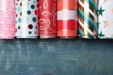 Photo of Different colorful wrapping paper rolls on light blue wooden table, flat lay. Space for text