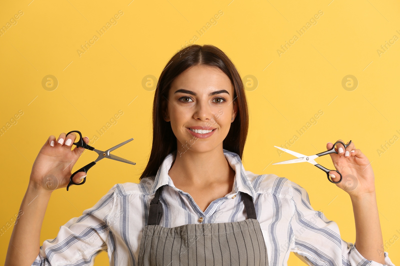 Photo of Young hairstylist holding professional scissors on color background