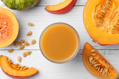 Photo of Tasty pumpkin juice in glass and different pumpkins on white wooden table, flat lay