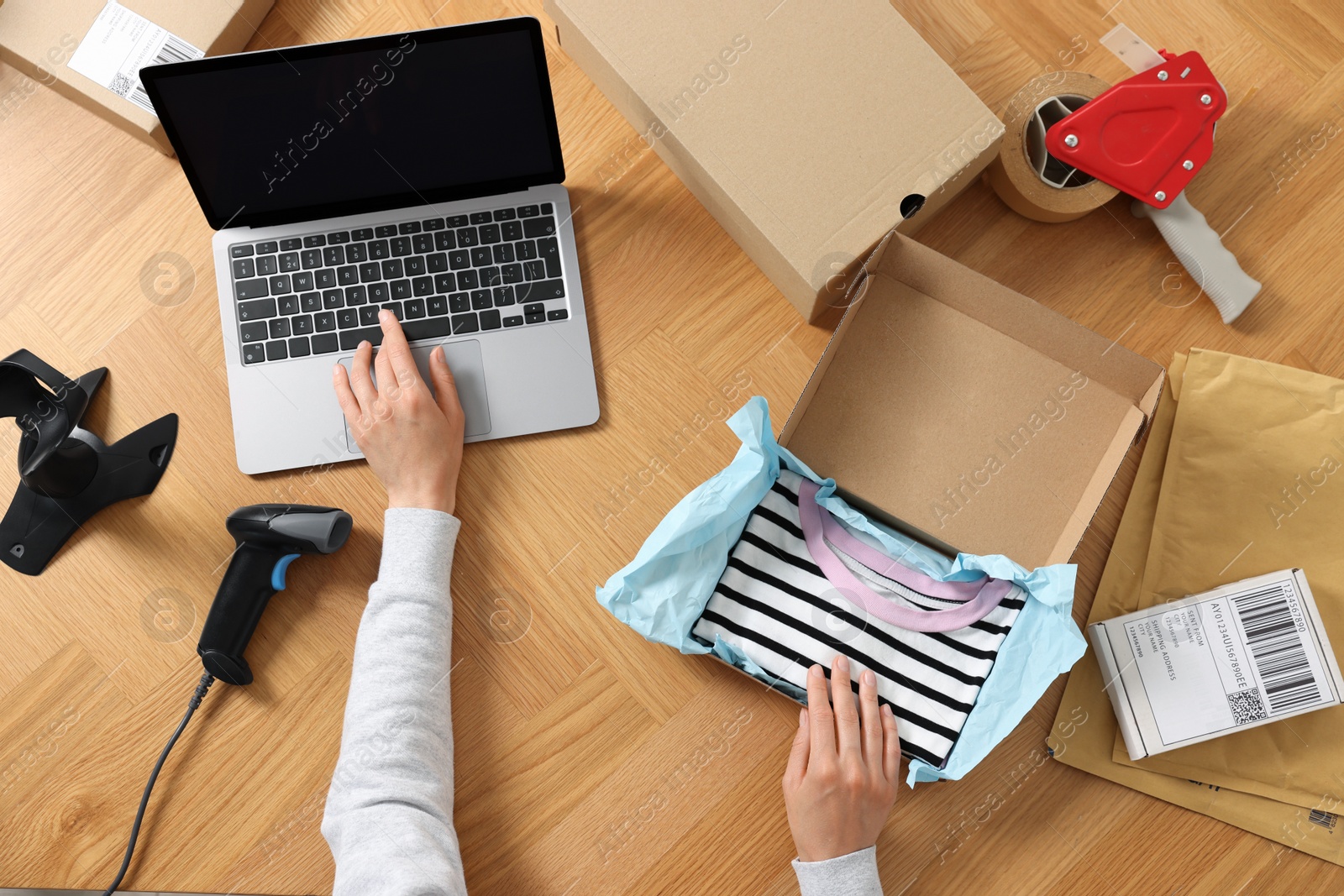 Photo of Woman with laptop and parcel working at wooden table, top view. Online store