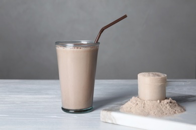 Photo of Glass with protein shake and scoop of powder on white wooden table