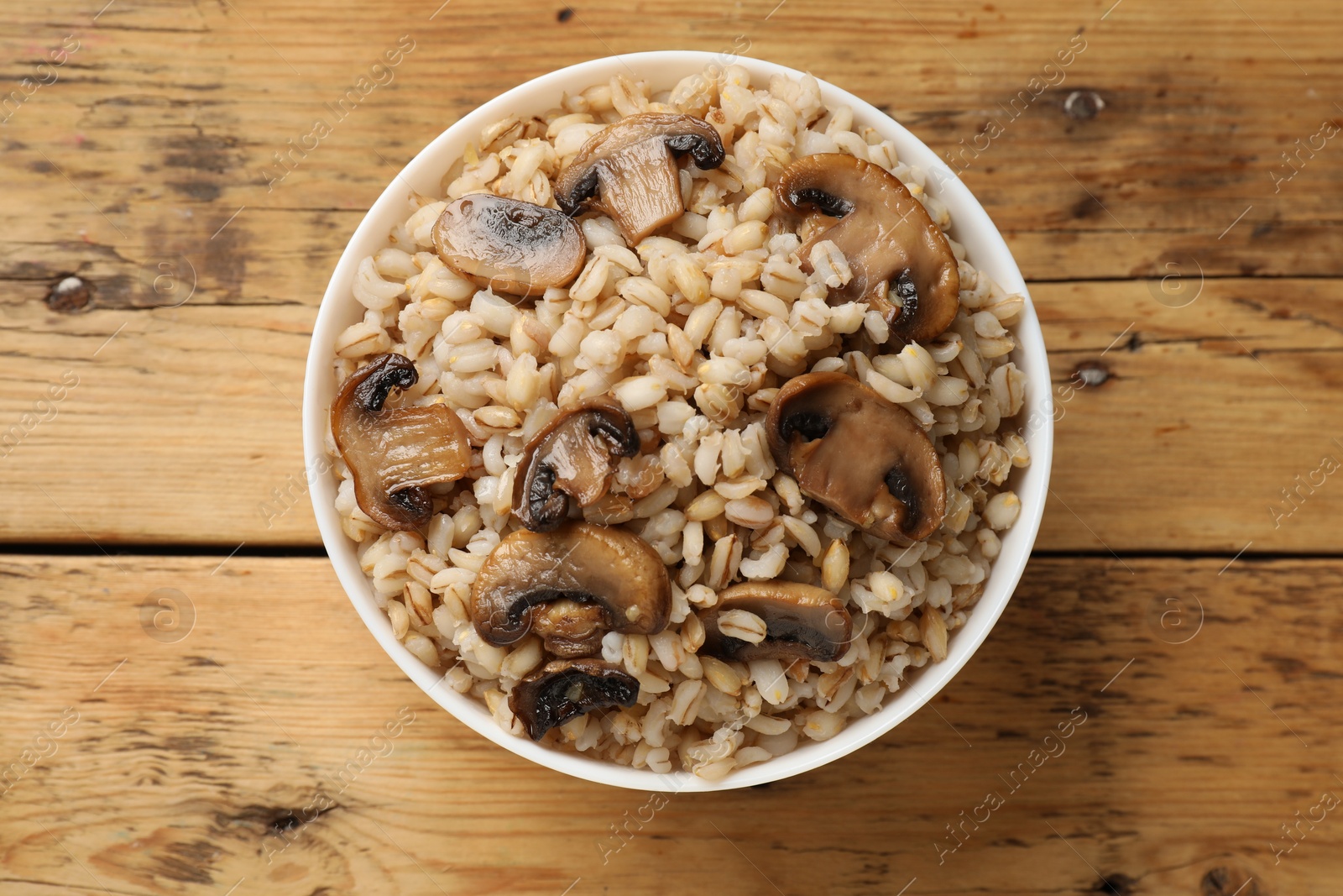 Photo of Delicious pearl barley with mushrooms in bowl on wooden table, top view