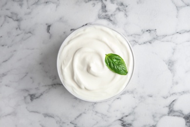 Photo of Bowl of fresh sour cream with basil on white marble table, top view