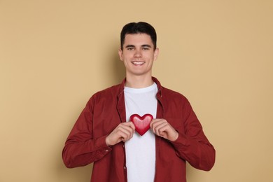 Happy volunteer holding red heart with hands on beige background