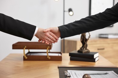 Photo of Notary shaking hands with client at wooden table in office, closeup