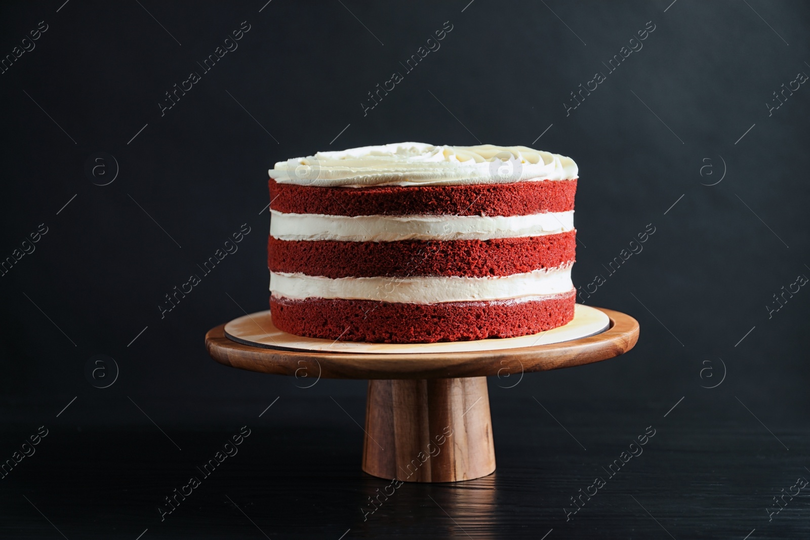 Photo of Delicious homemade red velvet cake on wooden stand against black background