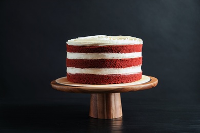 Photo of Delicious homemade red velvet cake on wooden stand against black background