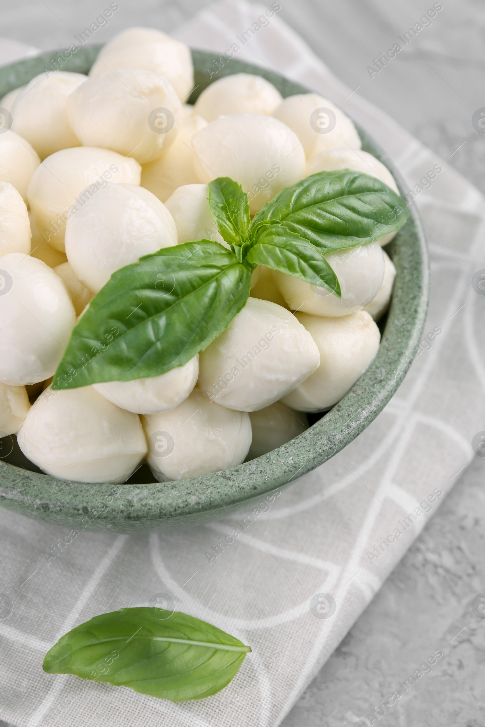 Photo of Tasty mozzarella balls and basil leaves in bowl on grey table
