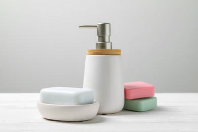 Soap bars and bottle dispenser on table against white background