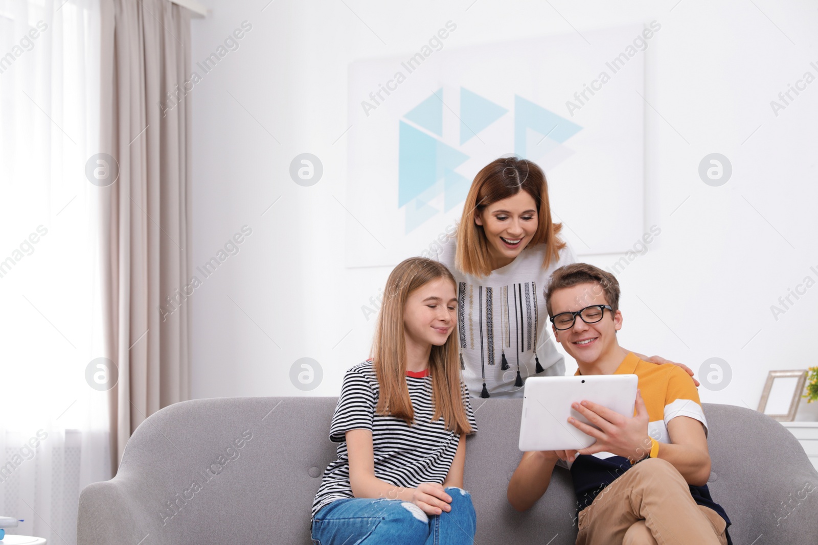 Photo of Happy mother, her teenager daughter and son with tablet at home