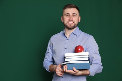 Photo of Portrait of young teacher with books and apple on green background. Space for text