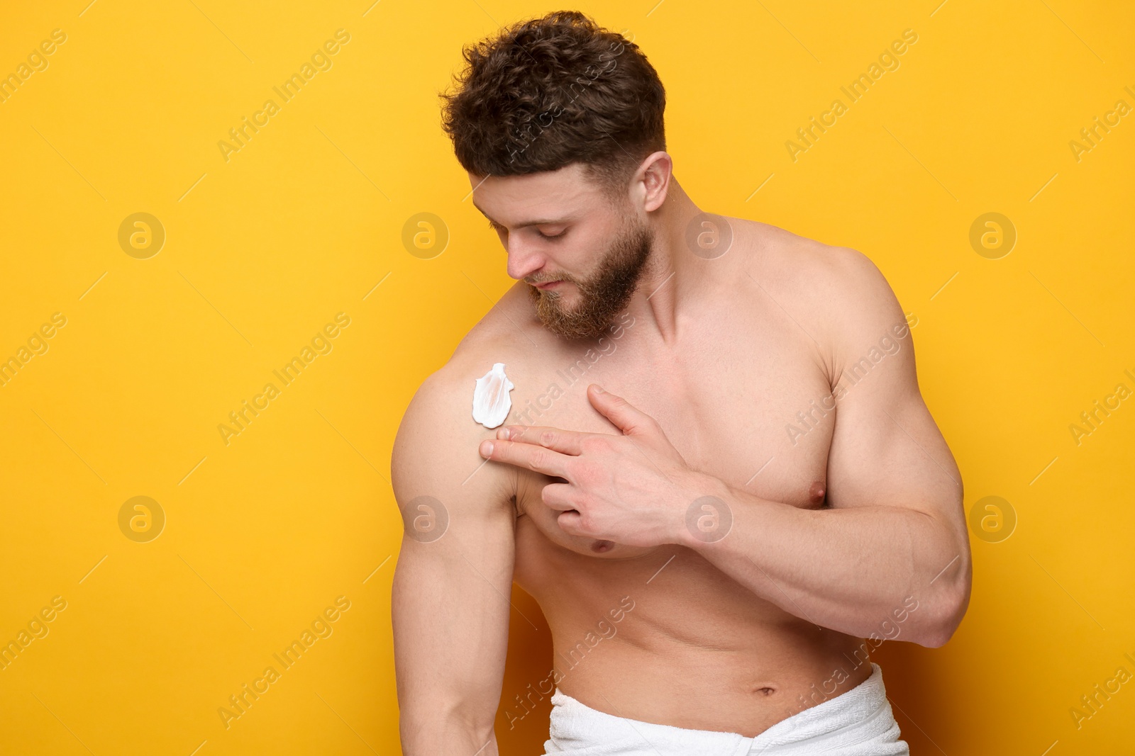Photo of Handsome man applying moisturizing cream onto his shoulder on orange background, space for text