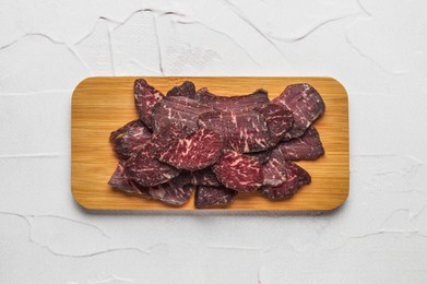 Pieces of delicious beef jerky on white textured table, top view