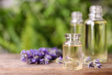 Photo of Bottles with natural lavender essential oil on wooden table against blurred background. Space for text