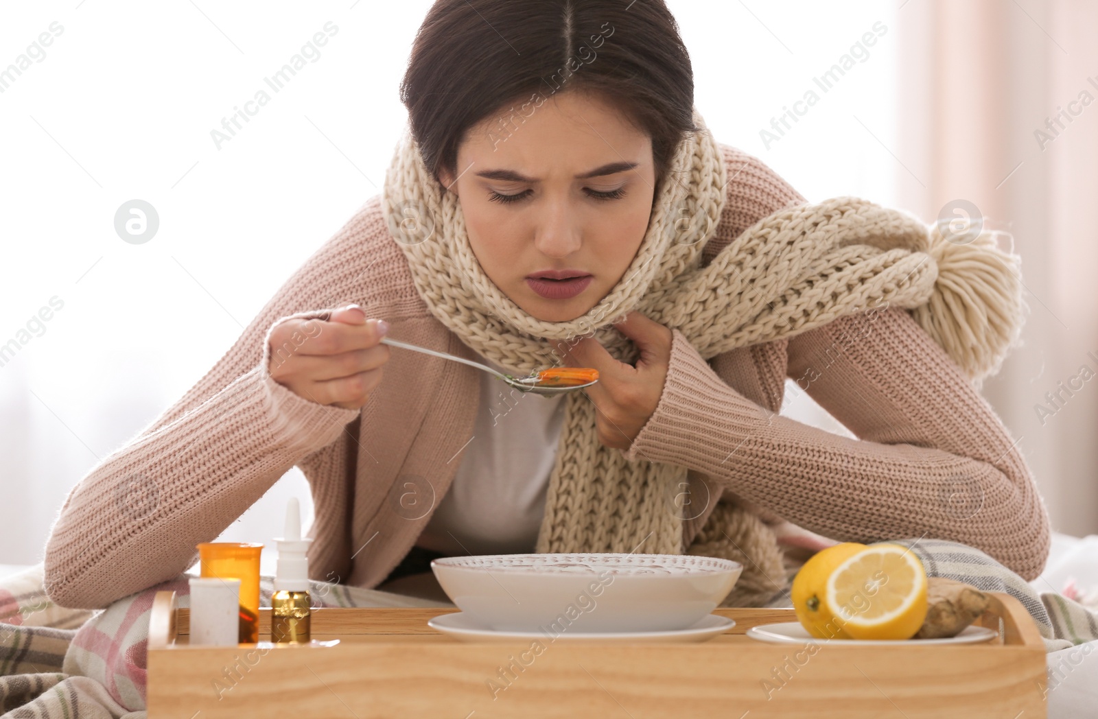 Photo of Sick young woman eating soup to cure flu at home