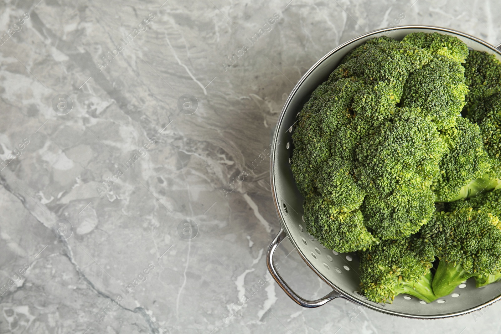 Photo of Fresh green broccoli in colander on grey marble table, top view. Space for text