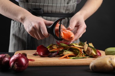 Photo of Woman peeling fresh carrot at black wooden table, closeup