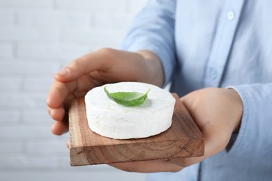 Woman holding serving board with delicious brie cheese on blurred background, closeup