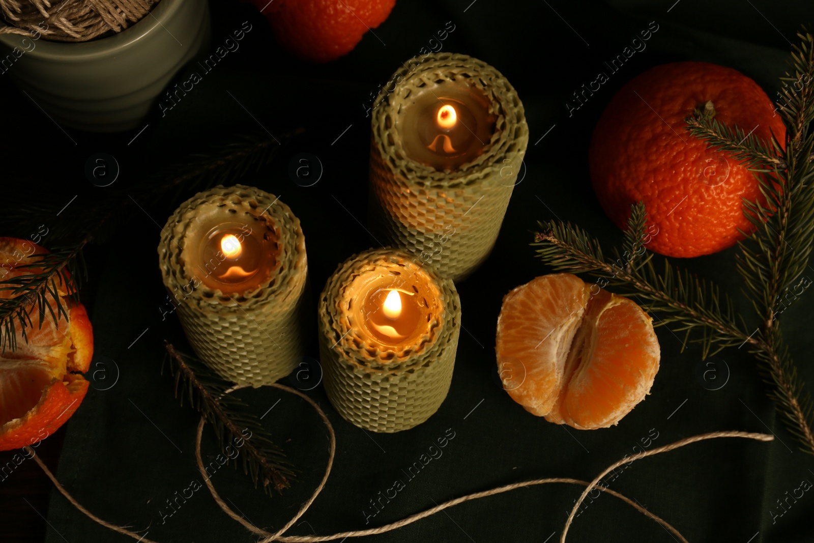 Photo of Beautiful burning beeswax candles, rope and tangerines on table, above view