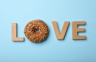 Word LOVE made with wooden letters and donut on light blue background, flat lay